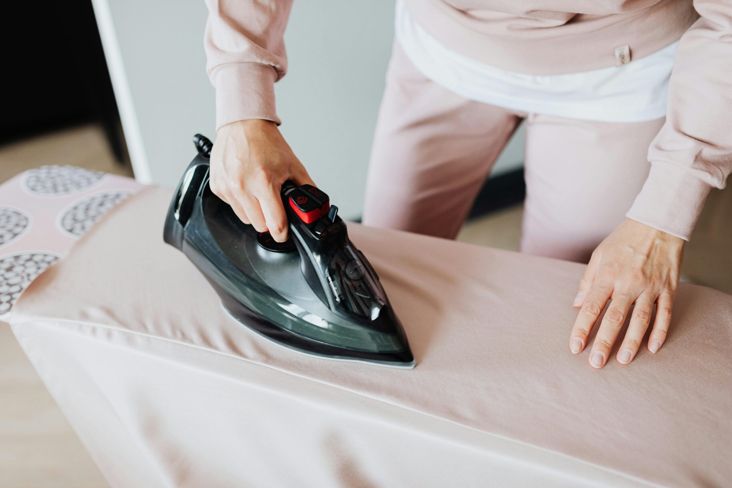 Adult woman ironing clothing on board using a black iron in an indoor setting.